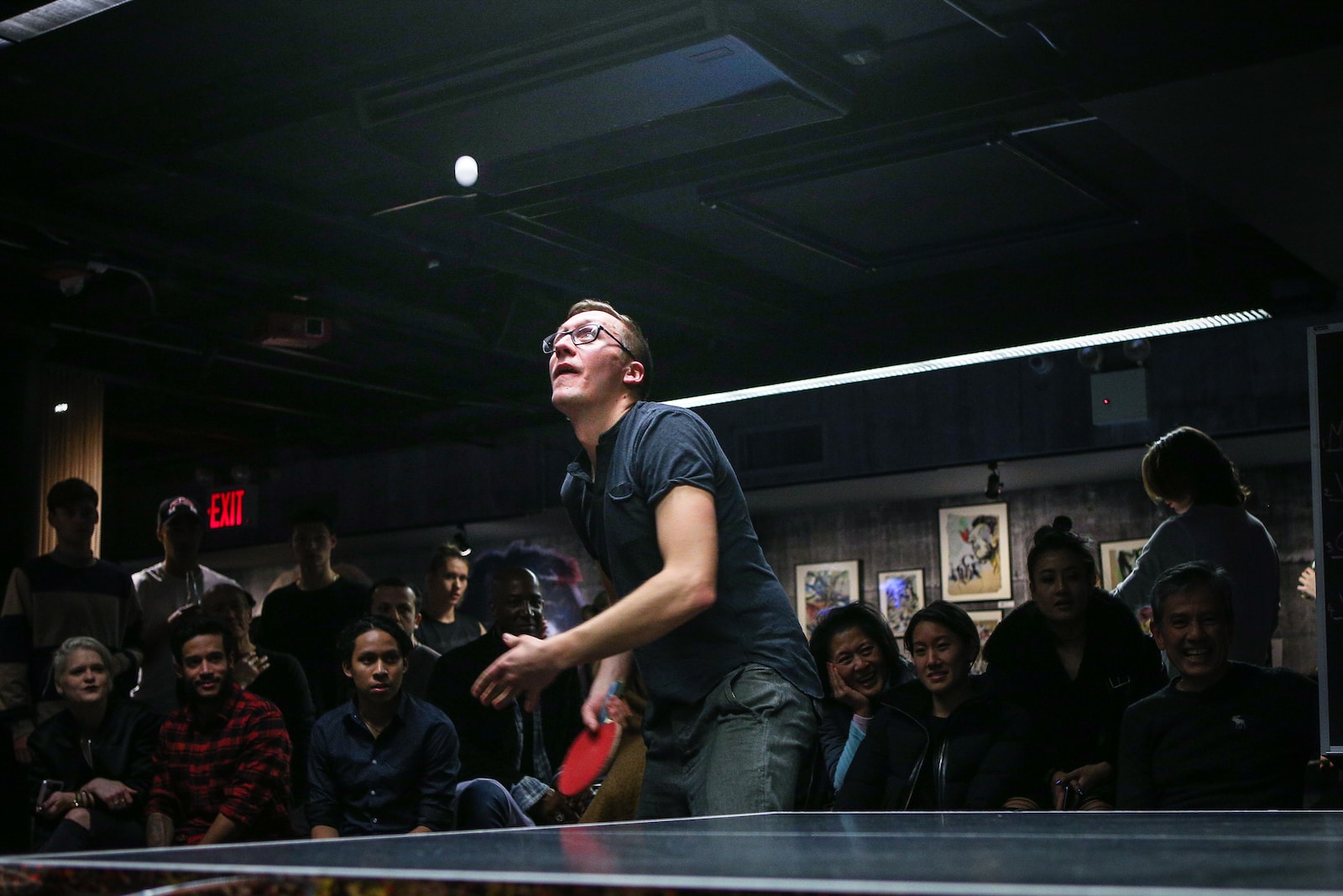 man about to paddle ping pong ball surrounded by group of people